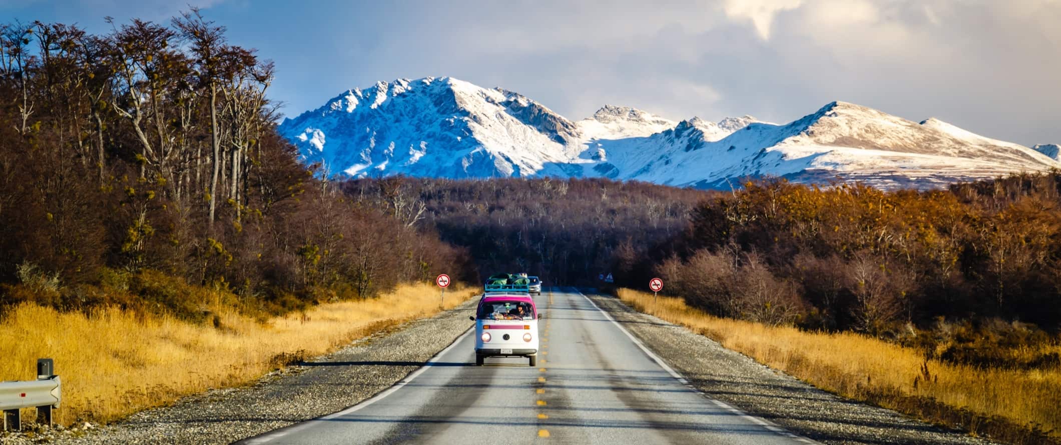 A vintage bus drives along a road against a dramatic mountainous backdrop in Argentina