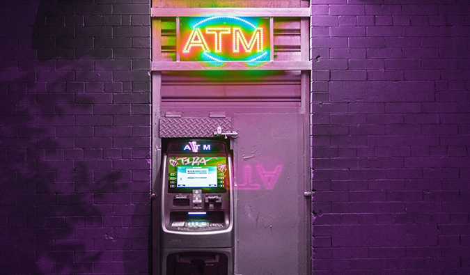 An ATM lit up at night against a purple brick wall
