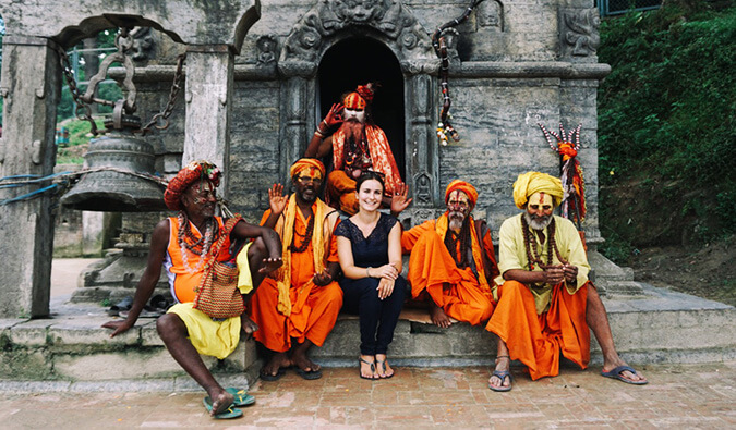 Woman sat outside a temple in India with 5 men dressed in traditional clothing and their faces painted