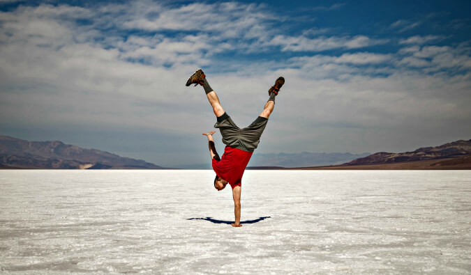 Man in wide open space with snow on the ground stood upside down on one hand