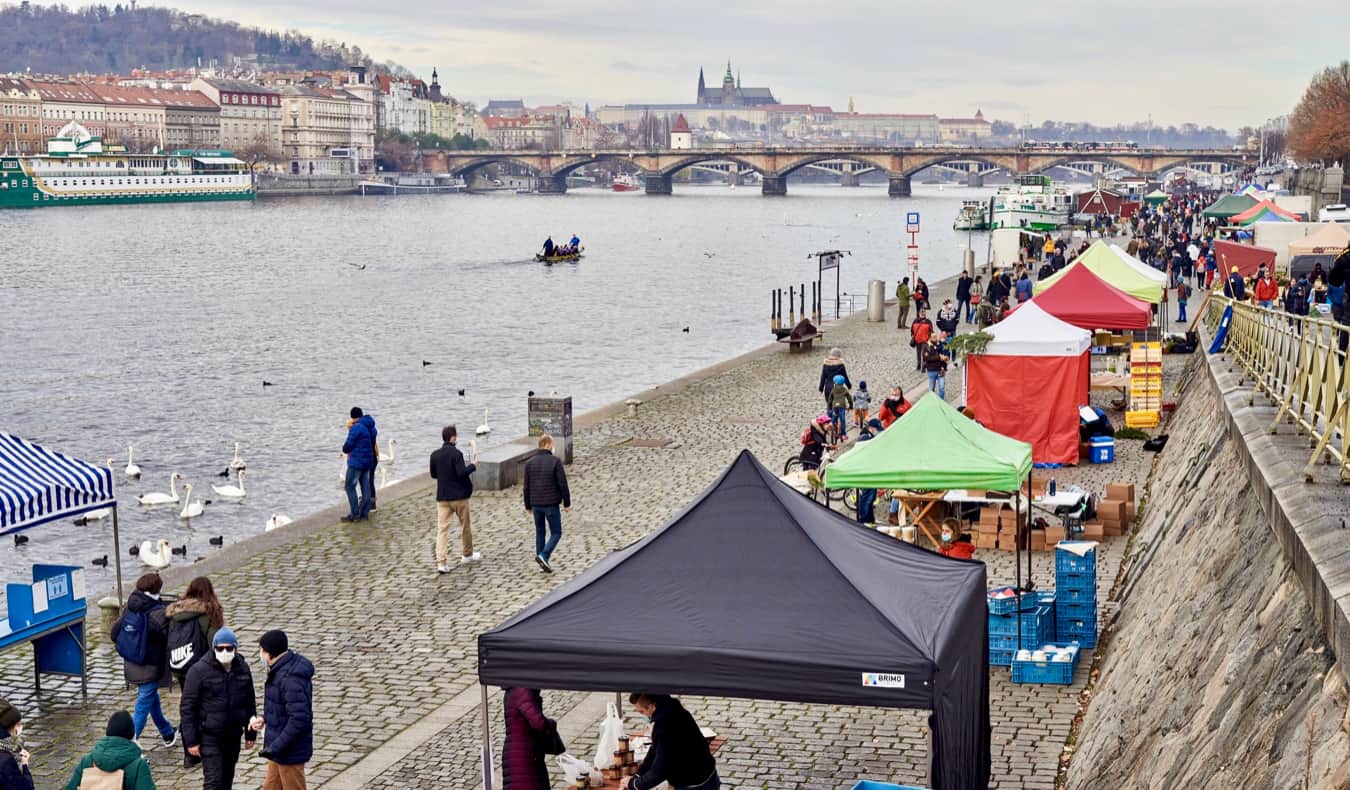 People walking near stalls along the river in Prague, Czechia