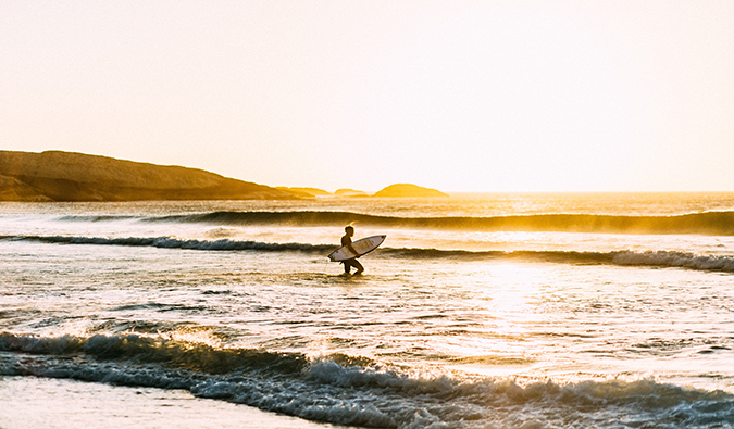 A lone traveler surfing in South Africa as the sun sets in the background