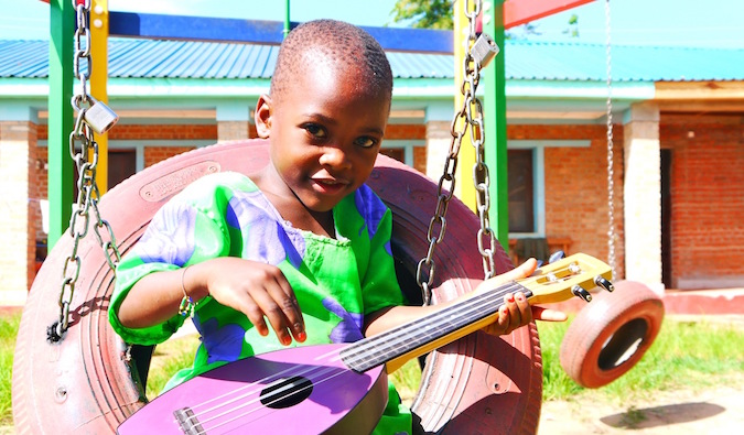 A young African child dressed in colorful clothing playing a small guitar