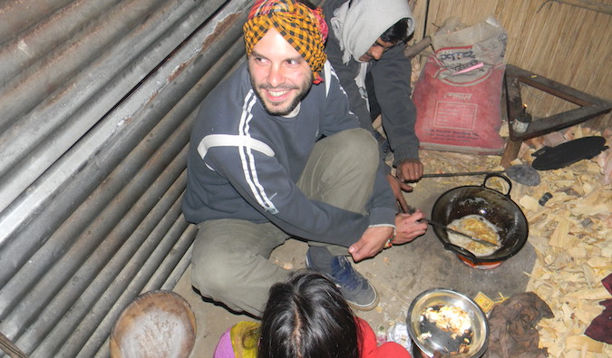 A solo traveler cooking with host family in a small hut overseas